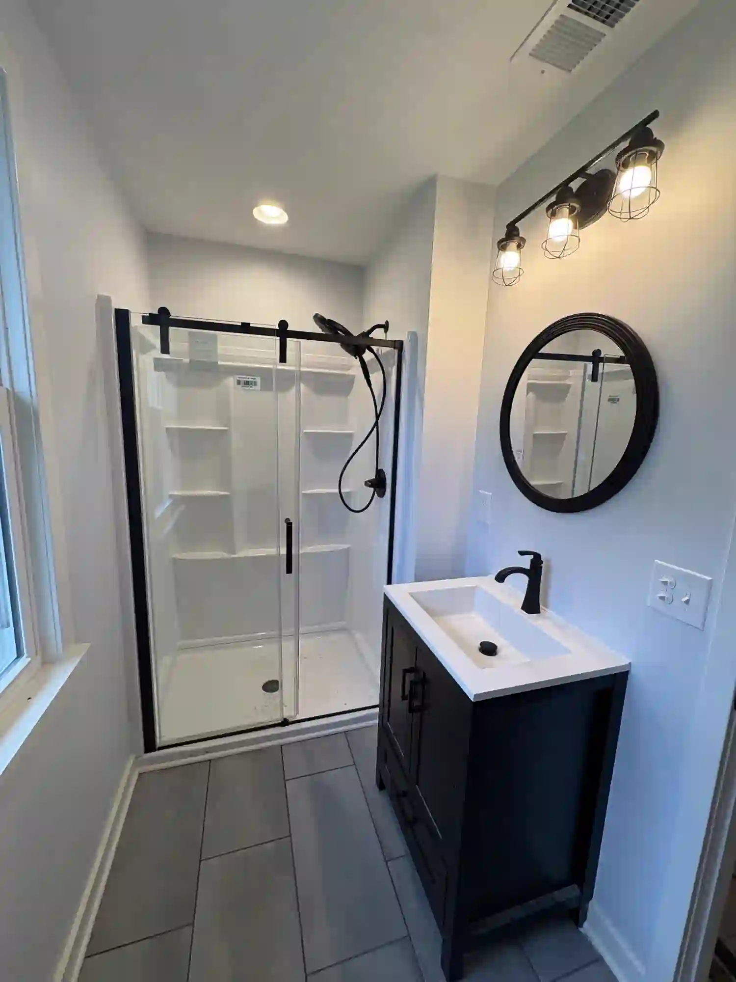 Finished guest bath with black vanity, round mirror, and industrial lighting