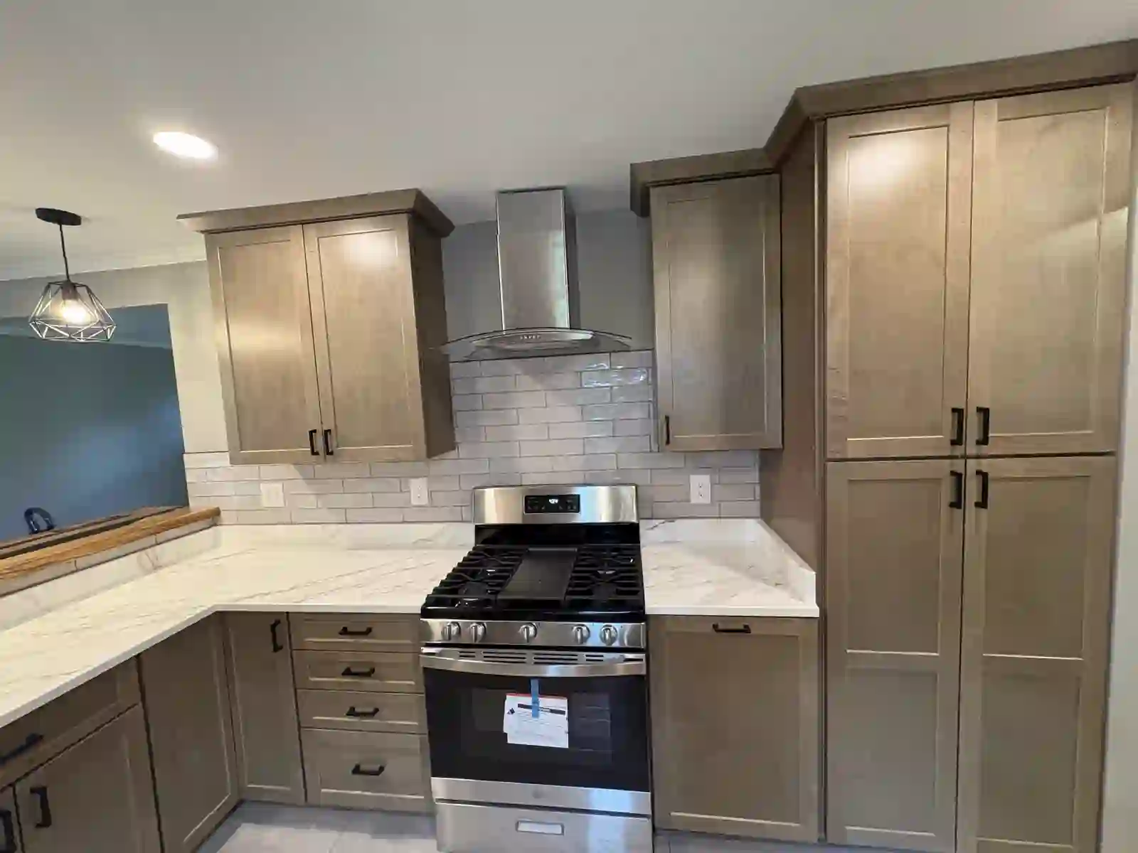 Finished kitchen with tan shaker cabinets, marble counters, gas range